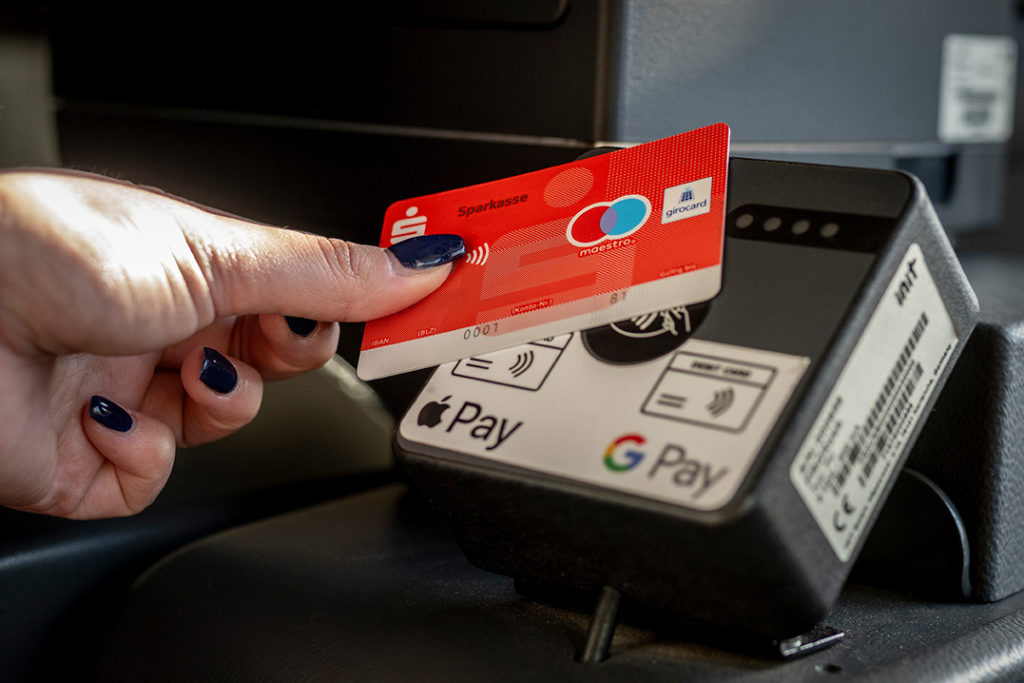 Eine Hand, die eine Girokarte an das Cashless-Terminal im HCR-Bus hält und damit bargeldlos bezahlt