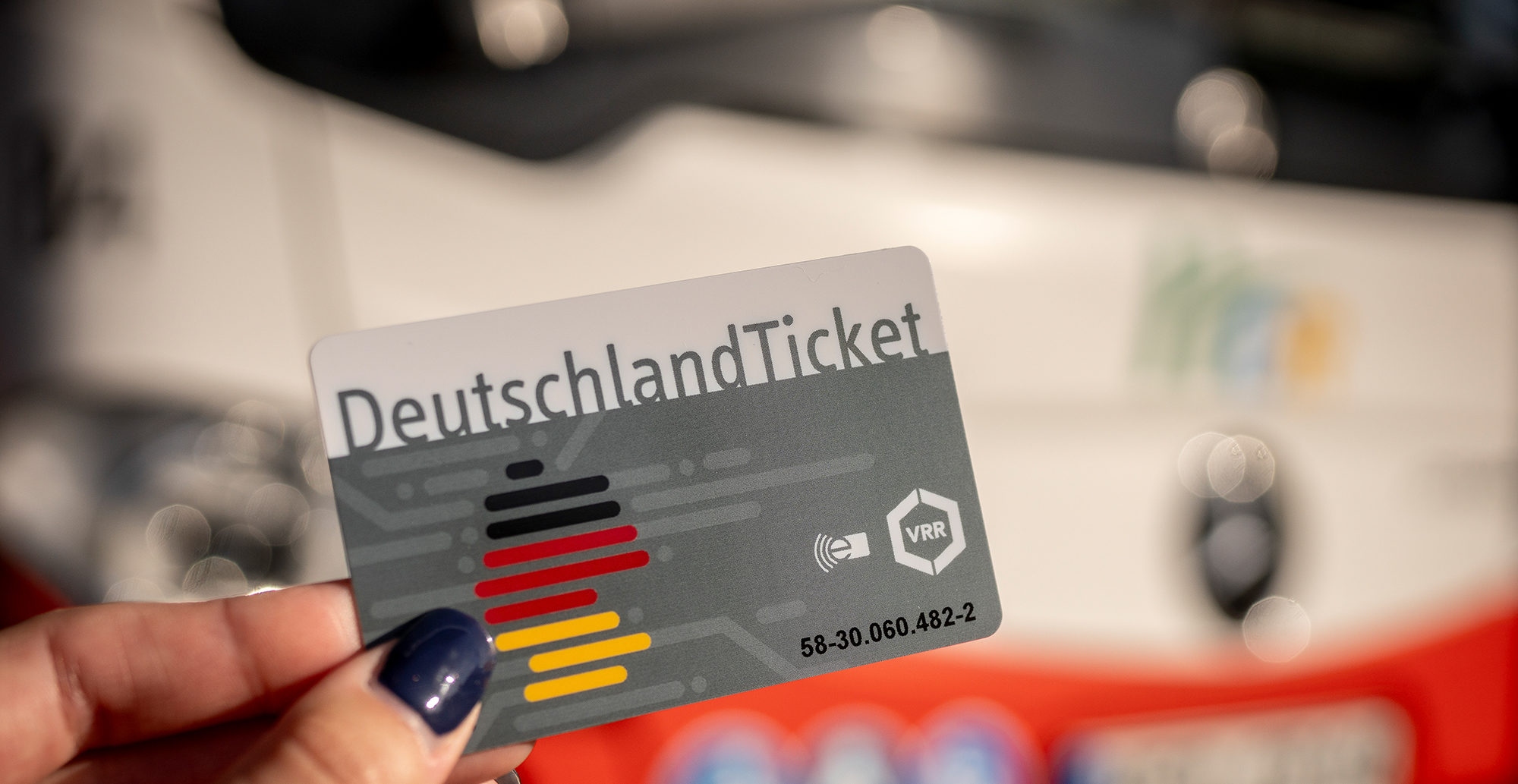Im Vordergrund hält eine Hand ein DeutschlandTicket. Im Hintergrund ist unscharf ein HCR-Bus zu sehen.