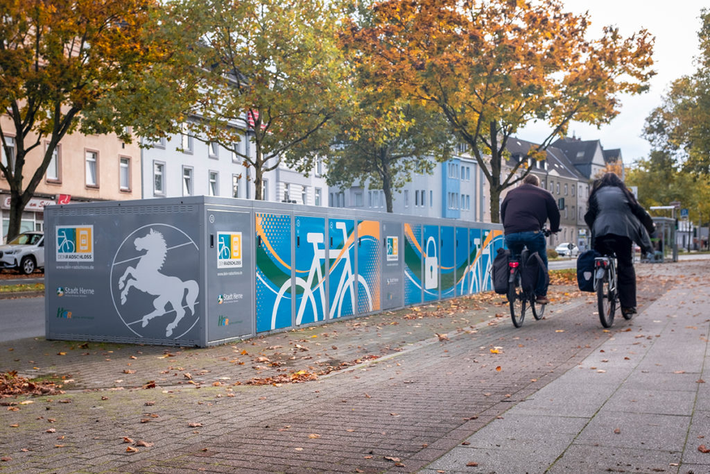 Zwei Radfahrer fahren an den Radboxen am Schloss Strünkede vorbei