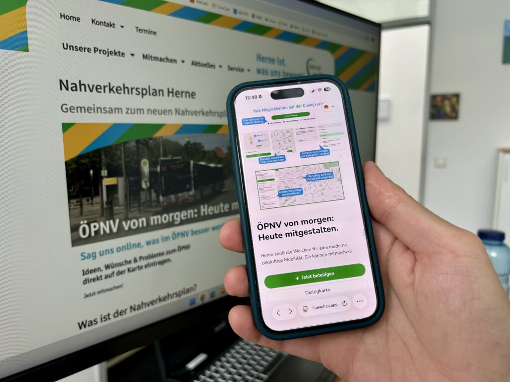 Ein Smartphone vor einem PC. Beide Geräte zeigen die Online-Beteiligung der Stadt Herne zum Nahverkehrsplan.