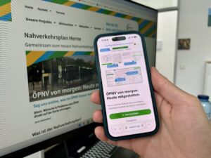 Ein Smartphone vor einem PC. Beide Geräte zeigen die Online-Beteiligung der Stadt Herne zum Nahverkehrsplan.