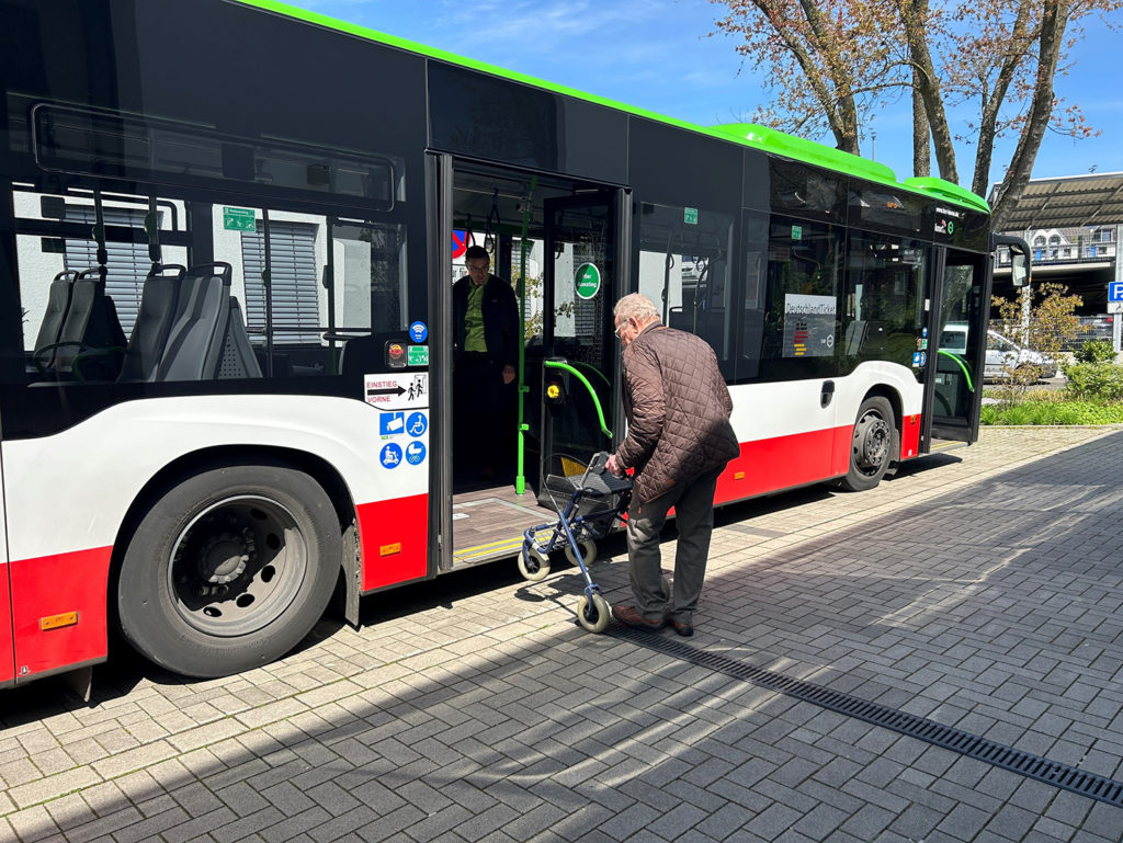 Ein älterer Herr übt beim Rollatorentraining der HCR den sicheren Einstieg in den Bus mit dem Rollator. Im Bus wird er angeleitet von einem HCR-Mitarbeiter.