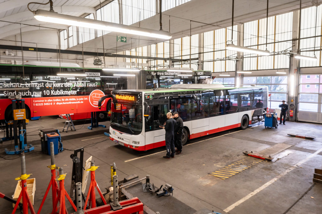 Blick von oben in die Werkstatt. Zwei Mitarbeitende sprechen vor einem Bus mit der Aufschrift "Werkstattfahrt" miteinander.