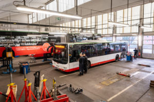 Blick von oben in die Werkstatt. Zwei Mitarbeitende sprechen vor einem Bus mit der Aufschrift "Werkstattfahrt" miteinander.